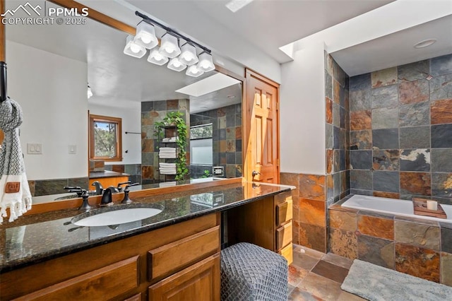 full bathroom with vanity, tiled bath, tile walls, and stone tile flooring
