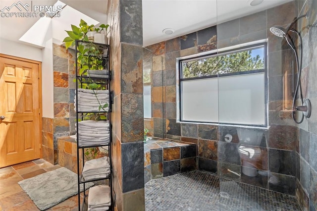 bathroom with stone tile floors, tile walls, and walk in shower
