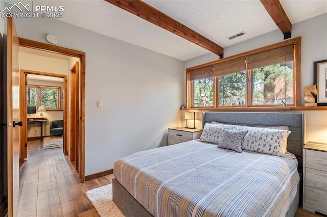 bedroom with visible vents, beam ceiling, multiple windows, and wood finished floors