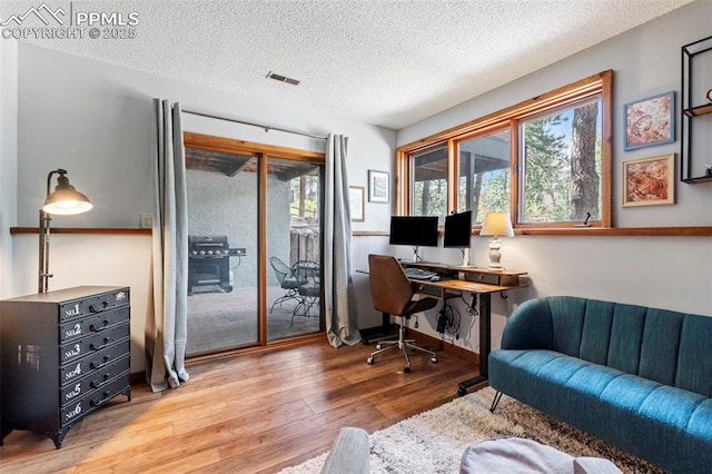 home office with a textured ceiling, wood finished floors, and visible vents