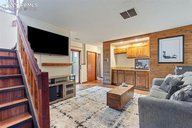 living area featuring wooden walls, visible vents, stairs, and light wood finished floors