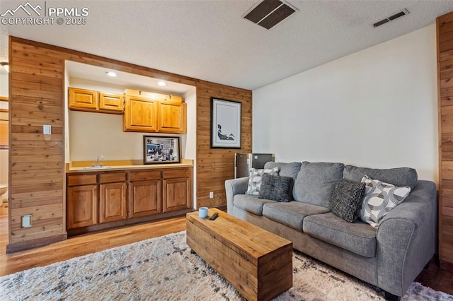 living room with light wood-style floors, wood walls, a textured ceiling, and visible vents
