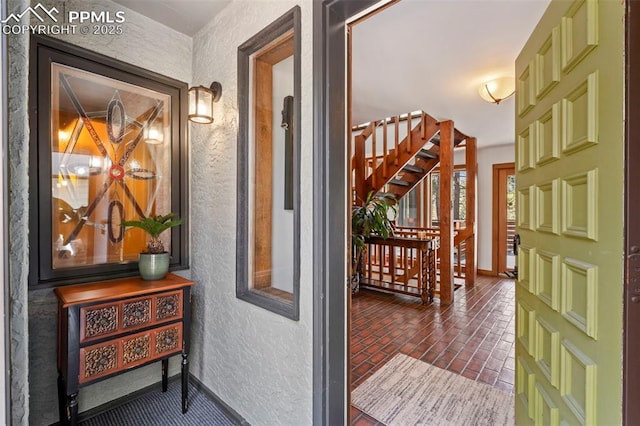 interior space featuring stairway, a textured wall, baseboards, and brick floor