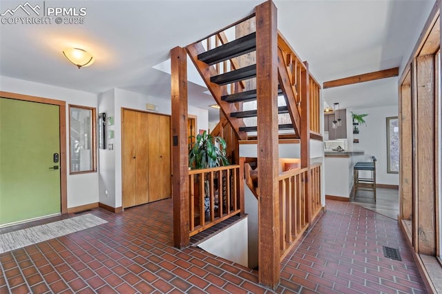 foyer featuring stairs, baseboards, visible vents, and brick floor