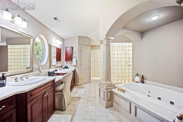 bathroom featuring vanity, visible vents, a jetted tub, ornate columns, and vaulted ceiling