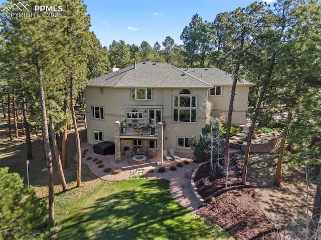 back of house featuring roof with shingles, a hot tub, stucco siding, a patio, and a yard