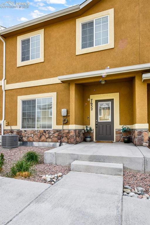 doorway to property with central AC unit, stucco siding, a porch, and stone siding
