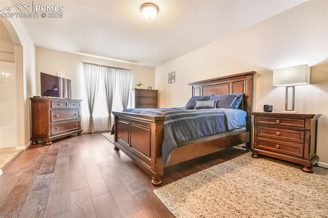bedroom with wood-type flooring, arched walkways, and baseboards