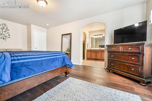 bedroom featuring ensuite bathroom, arched walkways, baseboards, and wood finished floors