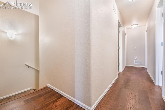 hallway with baseboards, visible vents, wood finished floors, and an upstairs landing