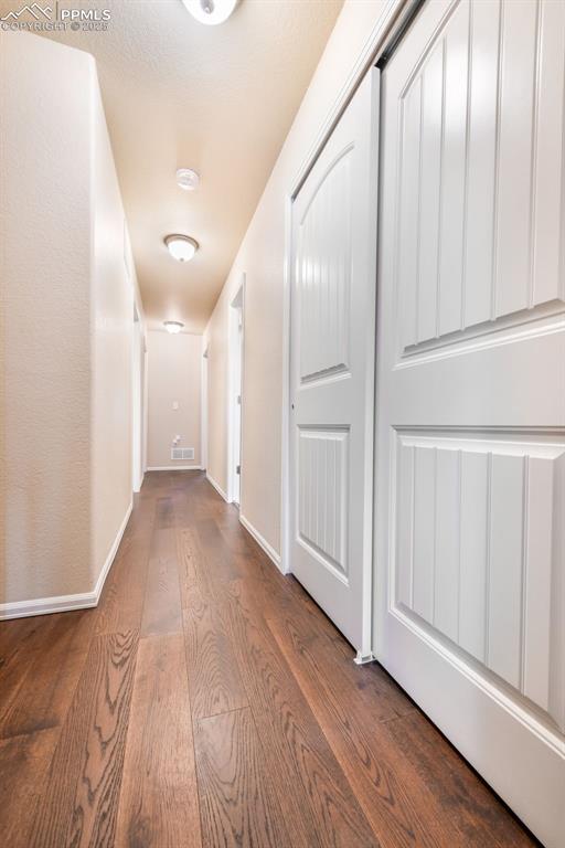 corridor with baseboards, wood finished floors, and visible vents