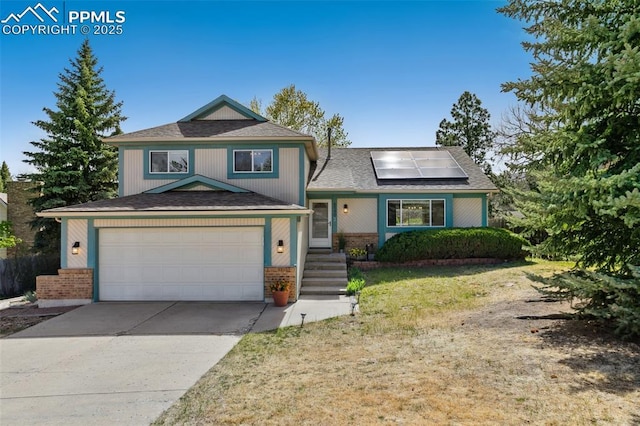 tri-level home featuring solar panels, roof with shingles, a garage, brick siding, and concrete driveway