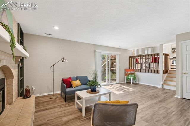 living room with visible vents, stairs, a brick fireplace, baseboards, and light wood-type flooring