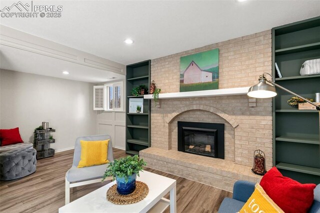 living area featuring baseboards, built in features, a brick fireplace, and wood finished floors
