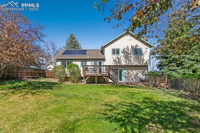 rear view of property with a lawn, a deck, roof mounted solar panels, a fenced backyard, and stairs