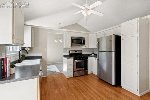kitchen with appliances with stainless steel finishes, dark countertops, a sink, light wood finished floors, and lofted ceiling