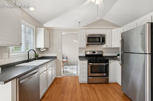 kitchen with a sink, dark countertops, vaulted ceiling, and stainless steel appliances