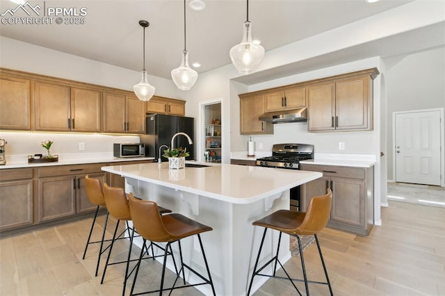 10323 Elevated Ln, Colorado Springs, CO 80924 - kitchen with a breakfast bar, under cabinet range hood, an island with sink, light countertops, and appliances with stainless steel finishes