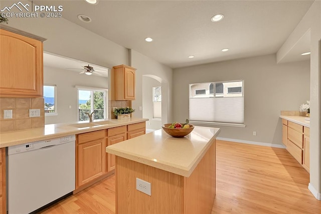 kitchen featuring decorative backsplash, white dishwasher, arched walkways, a sink, and light brown cabinets