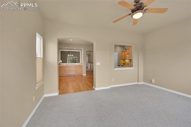 unfurnished room featuring arched walkways, baseboards, light carpet, and ceiling fan