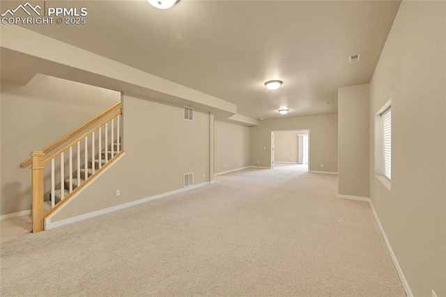 basement featuring visible vents, stairs, baseboards, and light colored carpet
