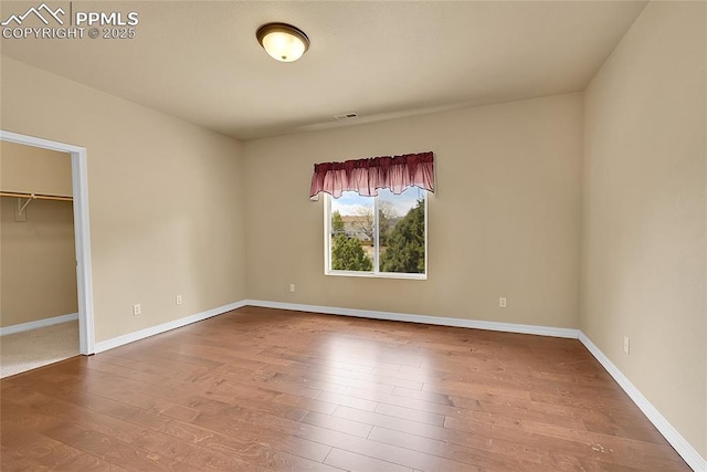 unfurnished bedroom featuring a walk in closet, baseboards, wood finished floors, visible vents, and a closet