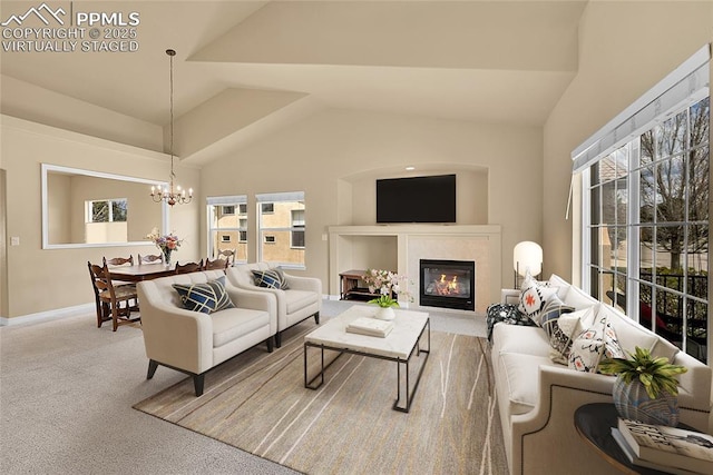 living area with a notable chandelier, a glass covered fireplace, a wealth of natural light, and lofted ceiling