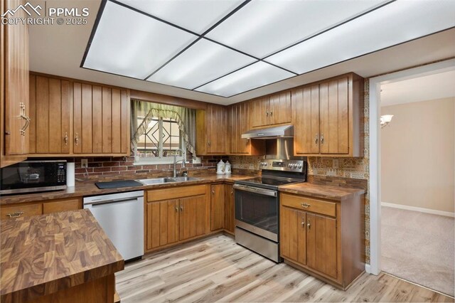 kitchen featuring a sink, butcher block countertops, brown cabinetry, stainless steel appliances, and under cabinet range hood