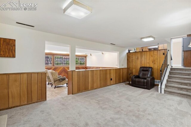 living area featuring visible vents, wainscoting, wood walls, light carpet, and stairs