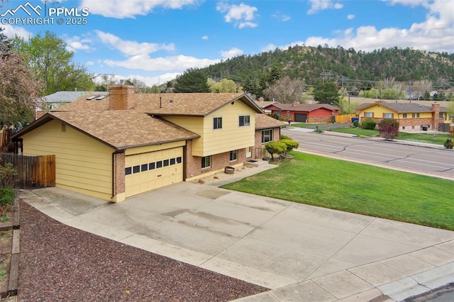 tri-level home featuring a chimney, brick siding, fence, a front lawn, and an attached garage