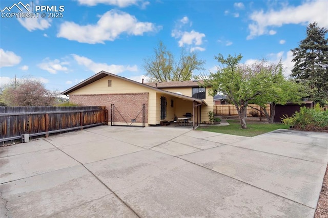 rear view of house with fence, brick siding, a patio area, concrete driveway, and an attached garage