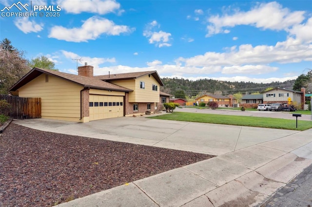 exterior space featuring fence, an attached garage, brick siding, a chimney, and concrete driveway