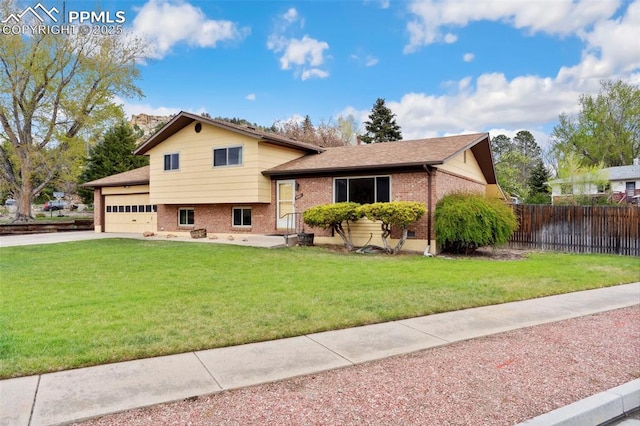 tri-level home with brick siding, a front lawn, an attached garage, and fence