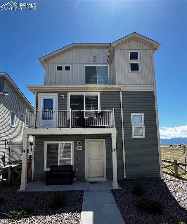 coastal inspired home featuring board and batten siding, a patio, fence, and a balcony