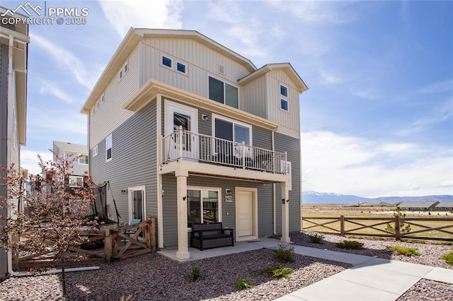 back of house with a balcony, board and batten siding, a mountain view, fence, and a patio area