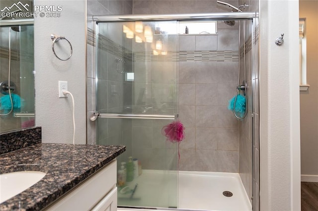 full bath with vanity, a shower stall, and a textured wall