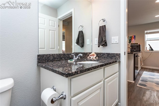 half bath featuring toilet, wood finished floors, baseboards, vanity, and recessed lighting