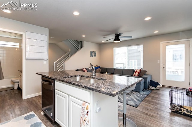 kitchen featuring a sink, dark stone counters, dishwasher, an island with sink, and a ceiling fan