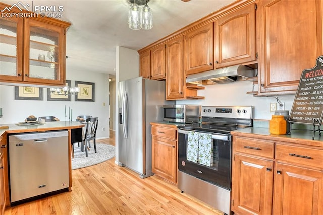 kitchen with under cabinet range hood, appliances with stainless steel finishes, brown cabinetry, and light wood-style floors
