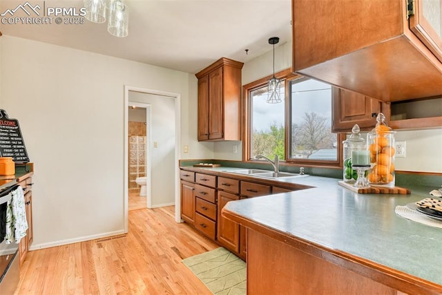 kitchen featuring electric range, a sink, brown cabinetry, decorative light fixtures, and light wood-type flooring