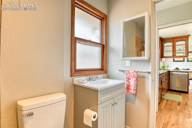 bathroom featuring toilet, a textured wall, wood finished floors, and vanity
