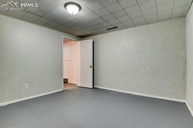 spare room featuring baseboards, a textured wall, and finished concrete floors