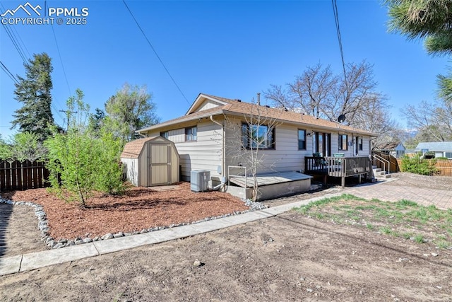 rear view of house featuring a deck, central AC, fence, an outdoor structure, and a storage unit