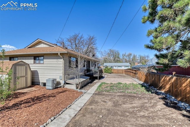 exterior space with a wooden deck, cooling unit, a fenced backyard, a storage unit, and an outbuilding
