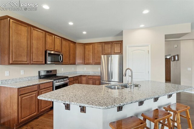 kitchen with brown cabinetry, a breakfast bar, a sink, dark wood finished floors, and appliances with stainless steel finishes