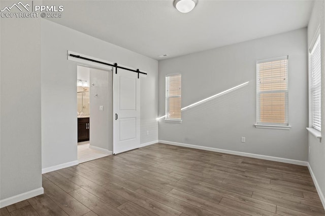 unfurnished bedroom with baseboards, a barn door, wood finished floors, and multiple windows