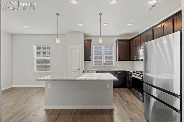 kitchen featuring dark brown cabinetry, appliances with stainless steel finishes, a sink, a kitchen island, and visible vents