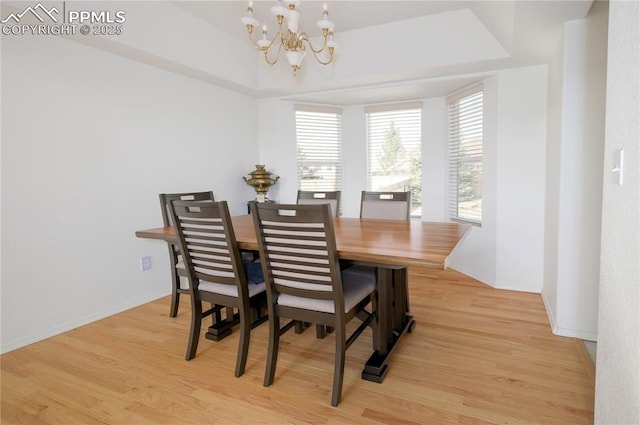 dining space featuring baseboards, a tray ceiling, light wood-type flooring, and a chandelier