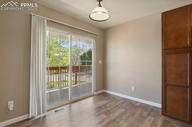 unfurnished dining area featuring baseboards, visible vents, and wood finished floors