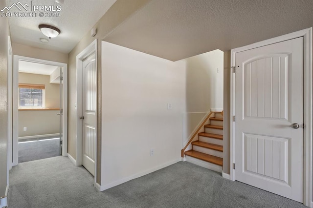 hallway featuring baseboards, carpet flooring, stairs, and a textured ceiling